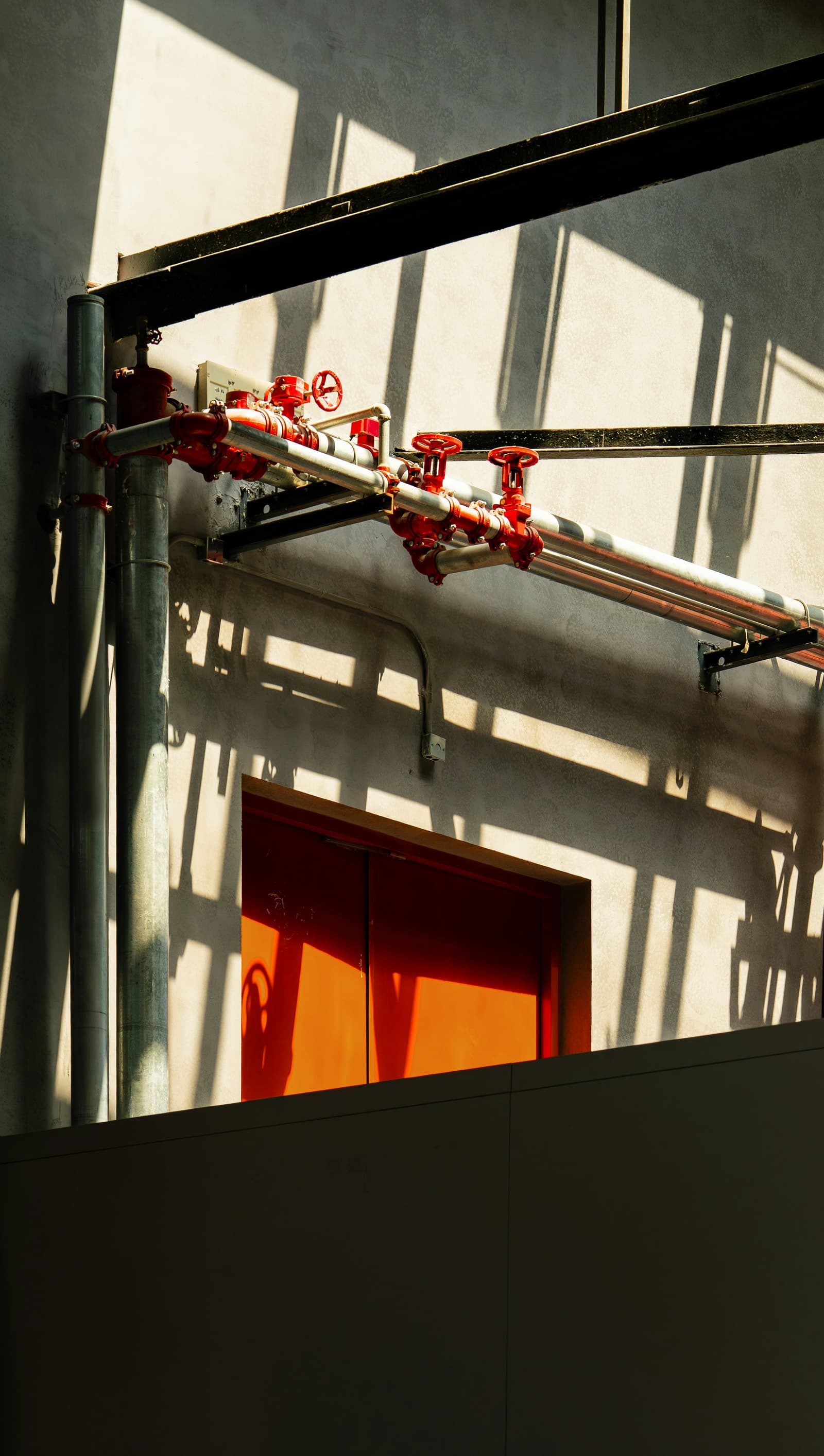 Industriële leidingen met rode afsluiters boven een oranje deur.